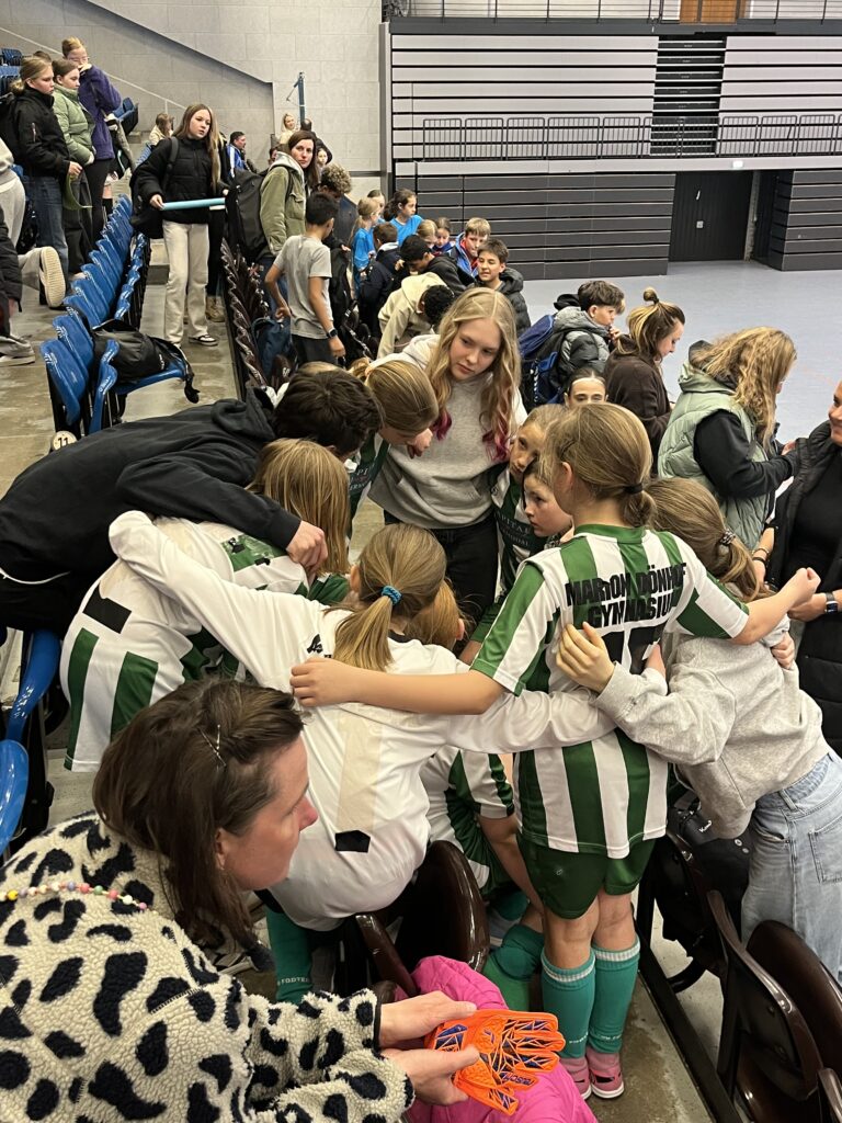 Eine Gruppe von Kindern in Sportkleidung umarmt sich freudig auf einer Tribüne.