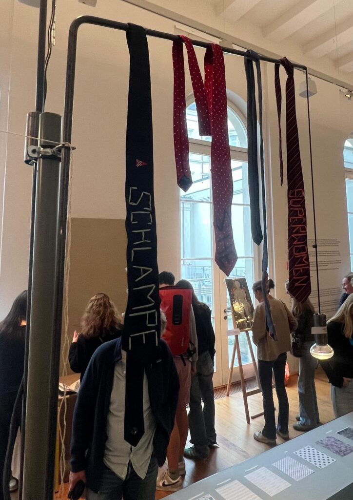 Eine Person mit einer Krawatte über dem Kopf steht in einem Ausstellungsraum.