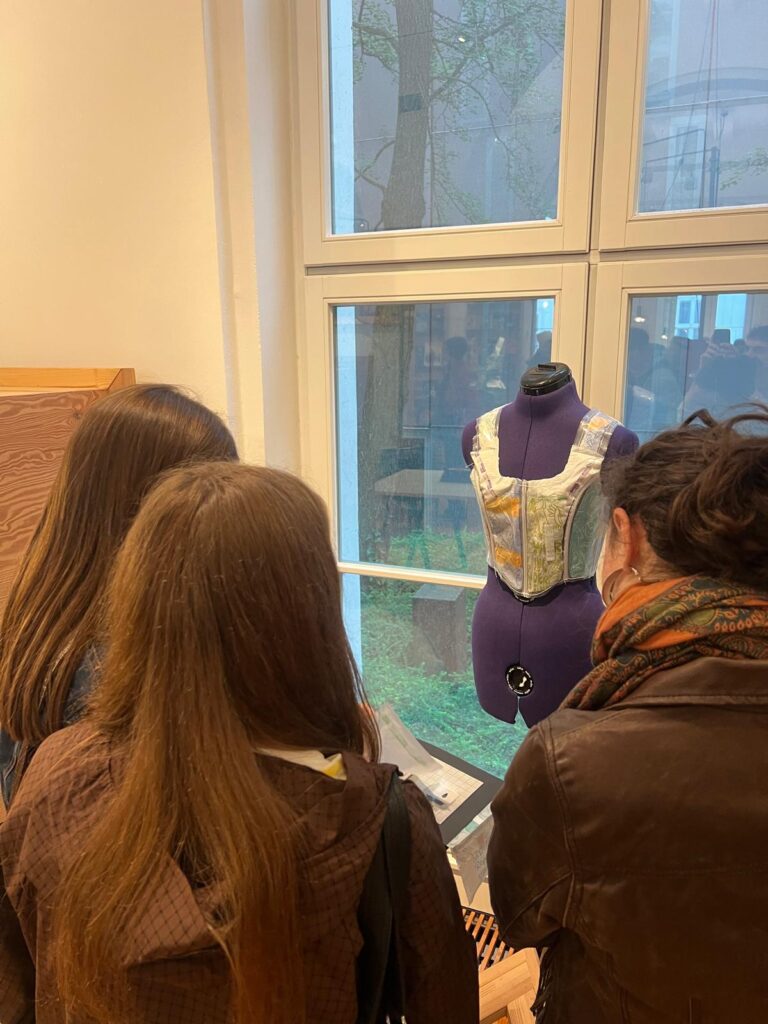 Drei Personen betrachten ein ausgestelltes Kleidungsstück auf einer Schneiderpuppe.