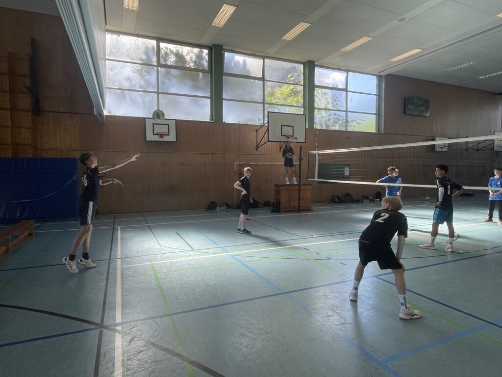 Zwei Jungen stehen auf dem Volleyballfeld, einer ist am Aufschlag, der andere bereit zum Annehmen.