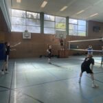 Zwei Jungen stehen auf dem Volleyballfeld, einer ist am Aufschlag, der andere bereit zum Annehmen.