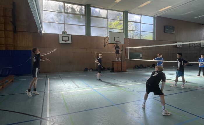Zwei Jungen stehen auf dem Volleyballfeld, einer ist am Aufschlag, der andere bereit zum Annehmen.