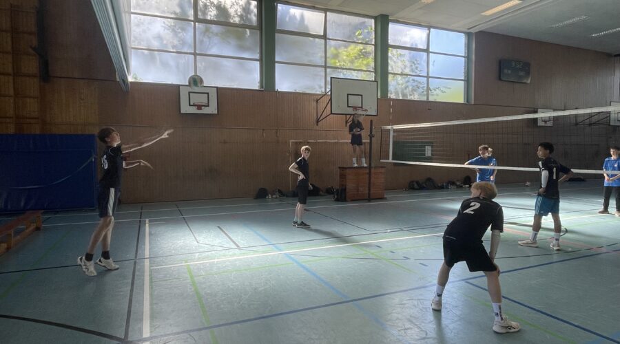 Zwei Jungen stehen auf dem Volleyballfeld, einer ist am Aufschlag, der andere bereit zum Annehmen.