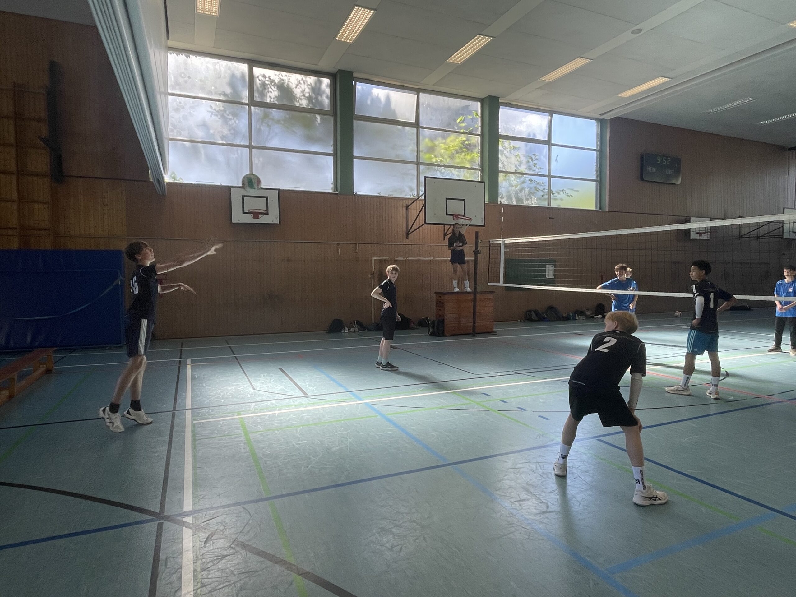 Zwei Jungen stehen auf dem Volleyballfeld, einer ist am Aufschlag, der andere bereit zum Annehmen.