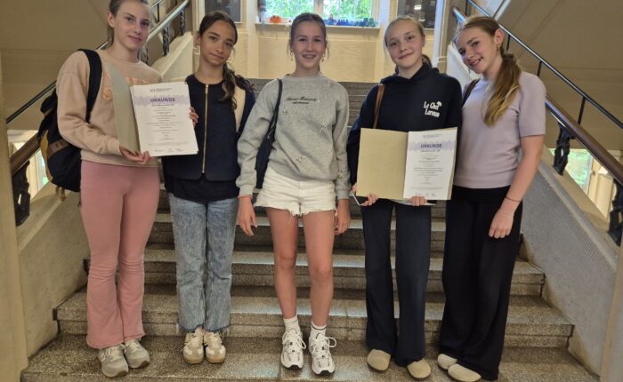 Fünf Jugendliche stehen lächelnd auf einer Treppe und halten Urkunden in der Hand.