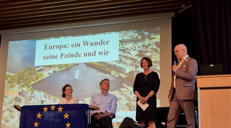 EinModerator spricht am Mikrofon vor einer Präsentation mit dem Titel „Europa: ein Wunder seine Feinde und wir“.
